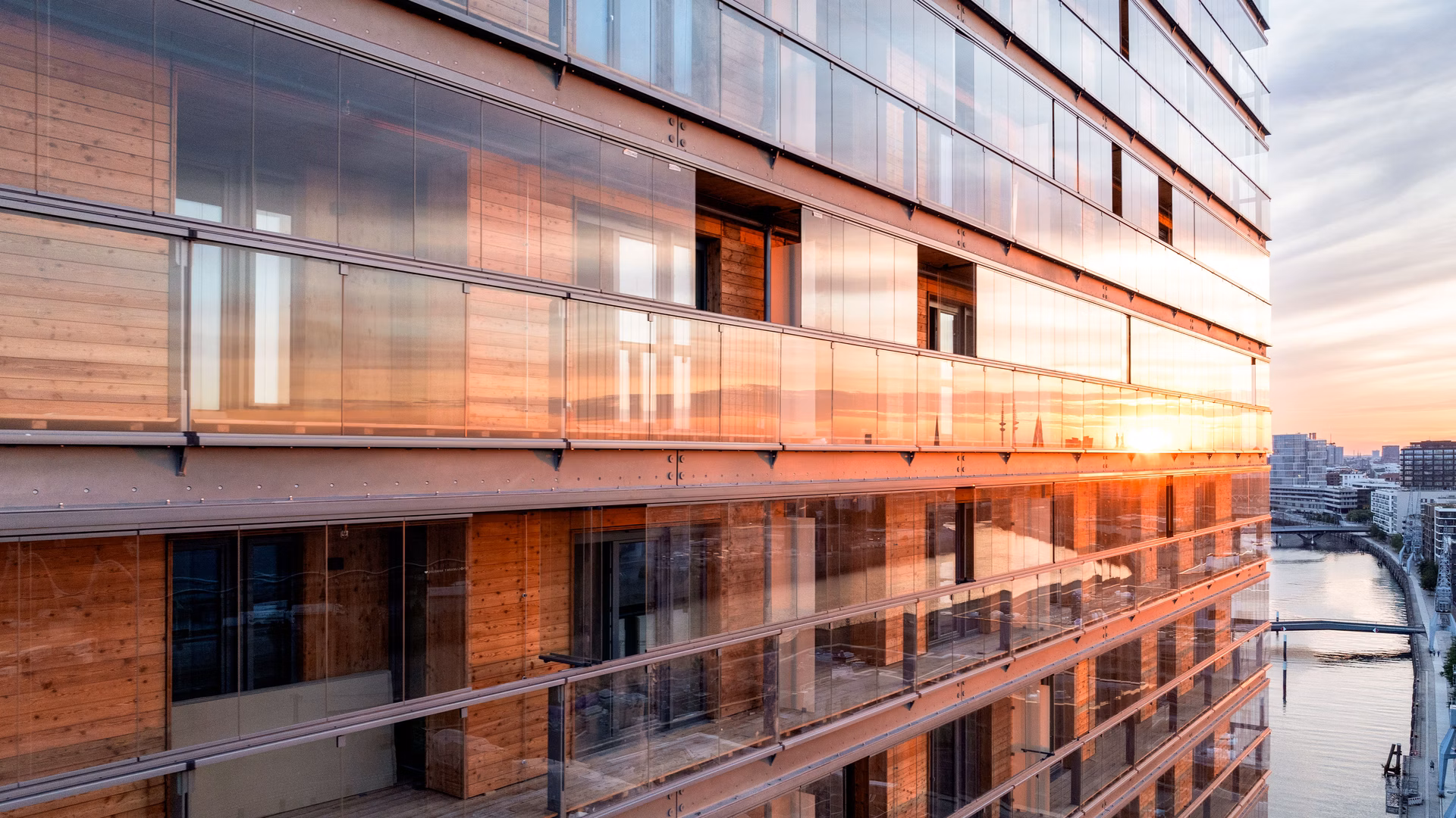 Mehrstöckige Holzfassade mit Glasbalkonen im Sonnenuntergang an einem Wasserkanal