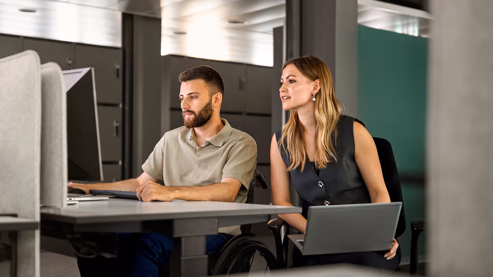 Two people are working on laptops in a modern office.