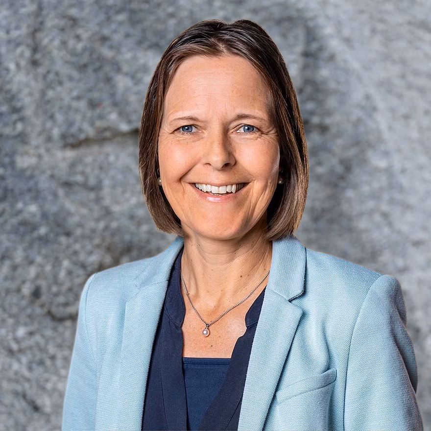 Portrait of a smiling woman in a light blue blazer against a grey background