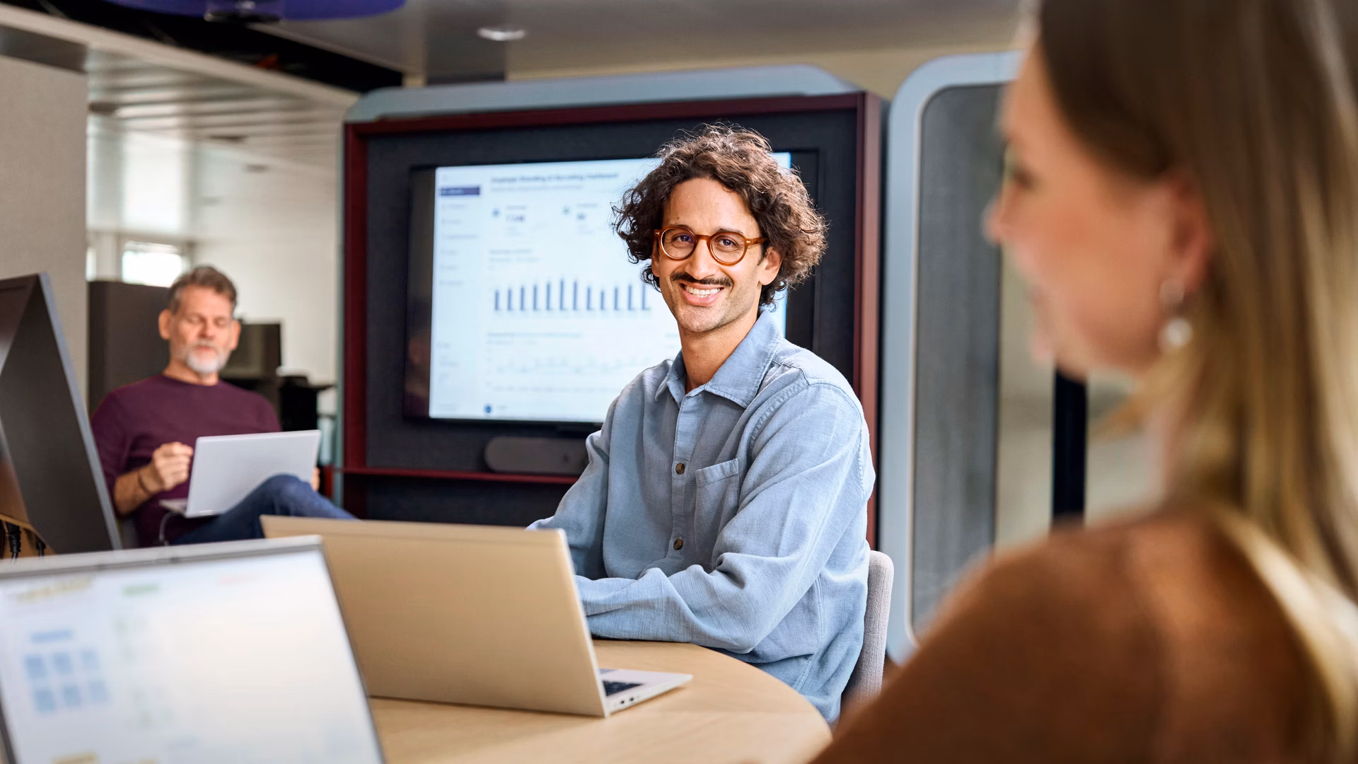 Employees in a meeting with laptops and a screen in a modern office.
