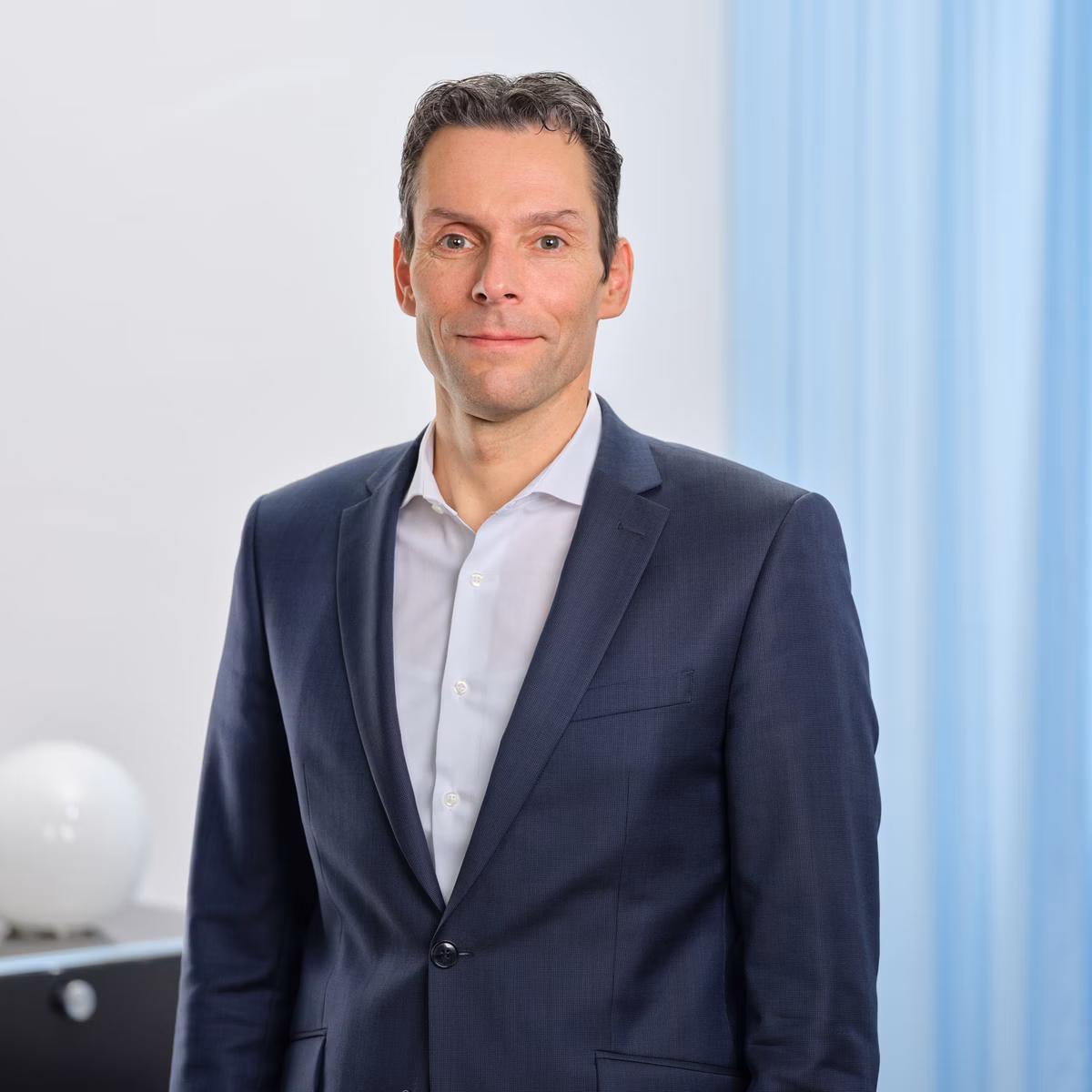 Andreas Ebner im blauen Anzug und weissem Hemd steht in einem hellen Büro.