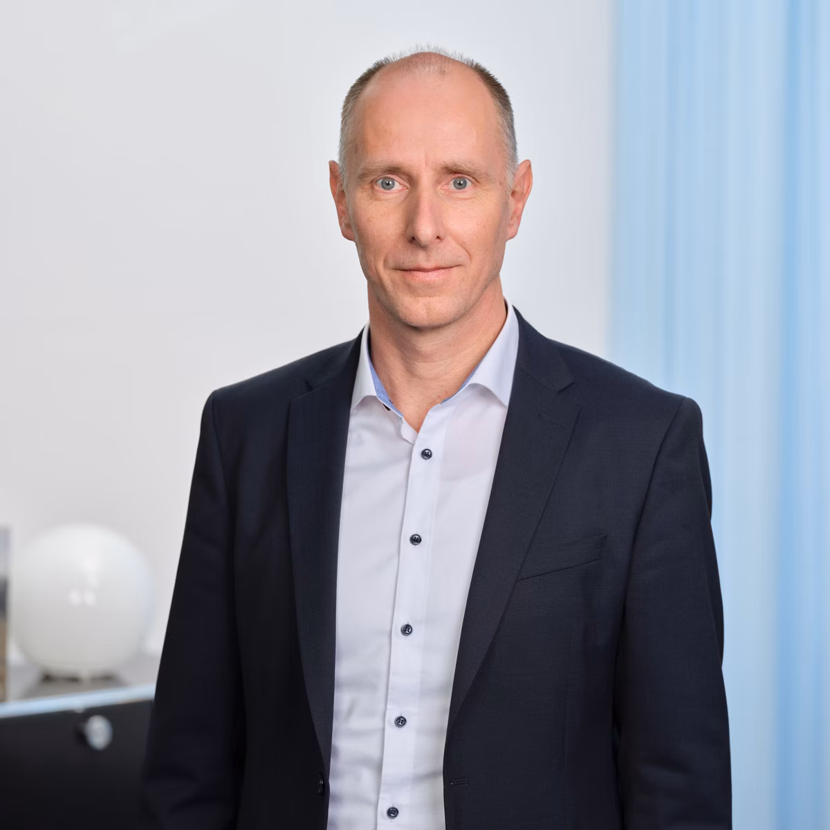 Stefan Witschi im dunklen Anzug und hellem Hemd steht in einem Büro vor hellem Hintergrund