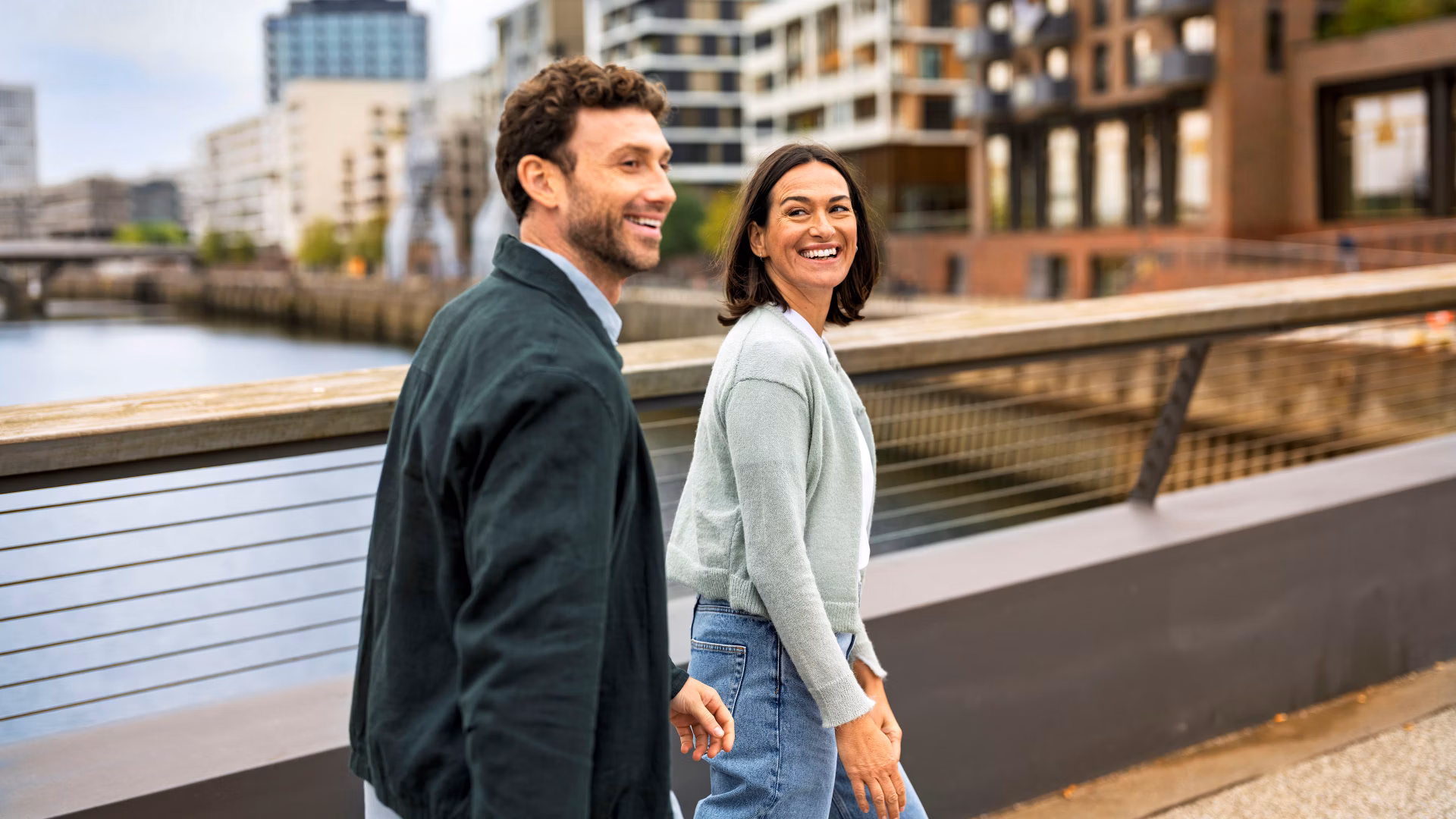 Two people are walking on a bridge in an urban neighbourhood by the water.