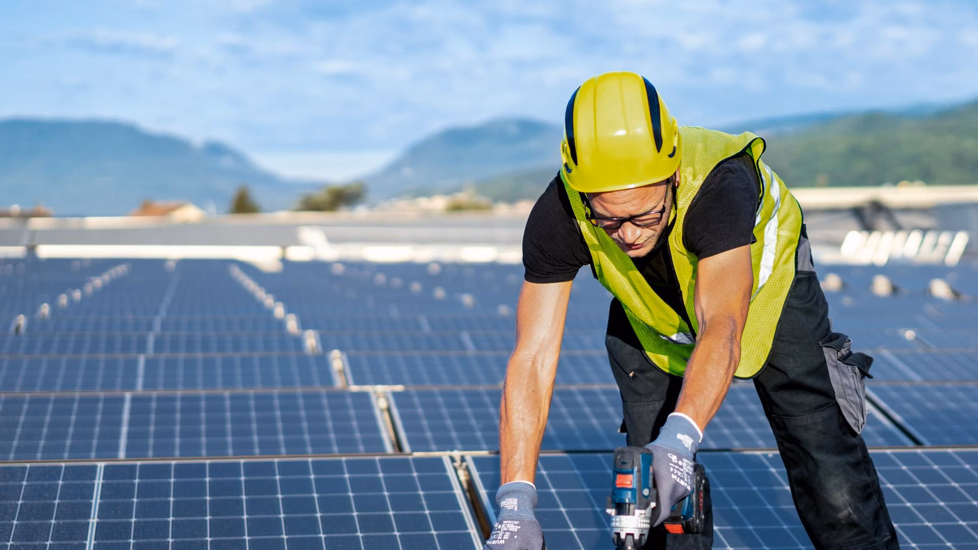 Un ouvrier portant un casque de protection et un gilet de signalisation installe des modules solaires sur un toit.
