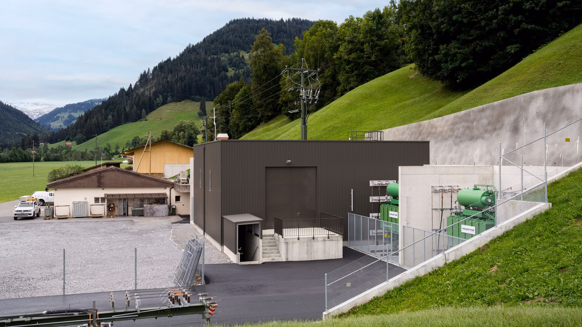 Kleines Industriegebäude mit technischer Anlage in einer grünen Hügellandschaft.
