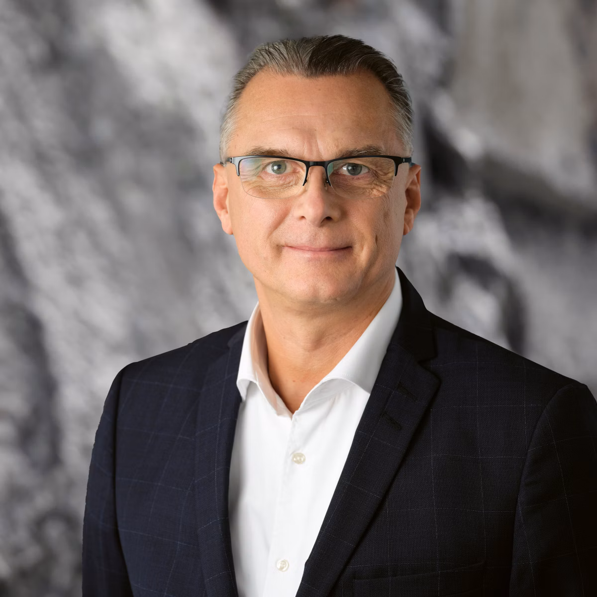 Man with glasses in a dark suit against a grey background