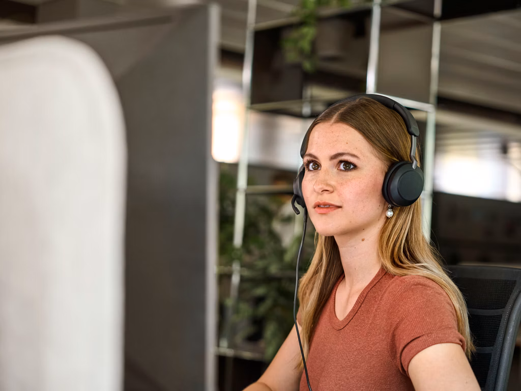 Junge Frau mit Kopfhörern an einem Computerarbeitsplatz in einem Büro.