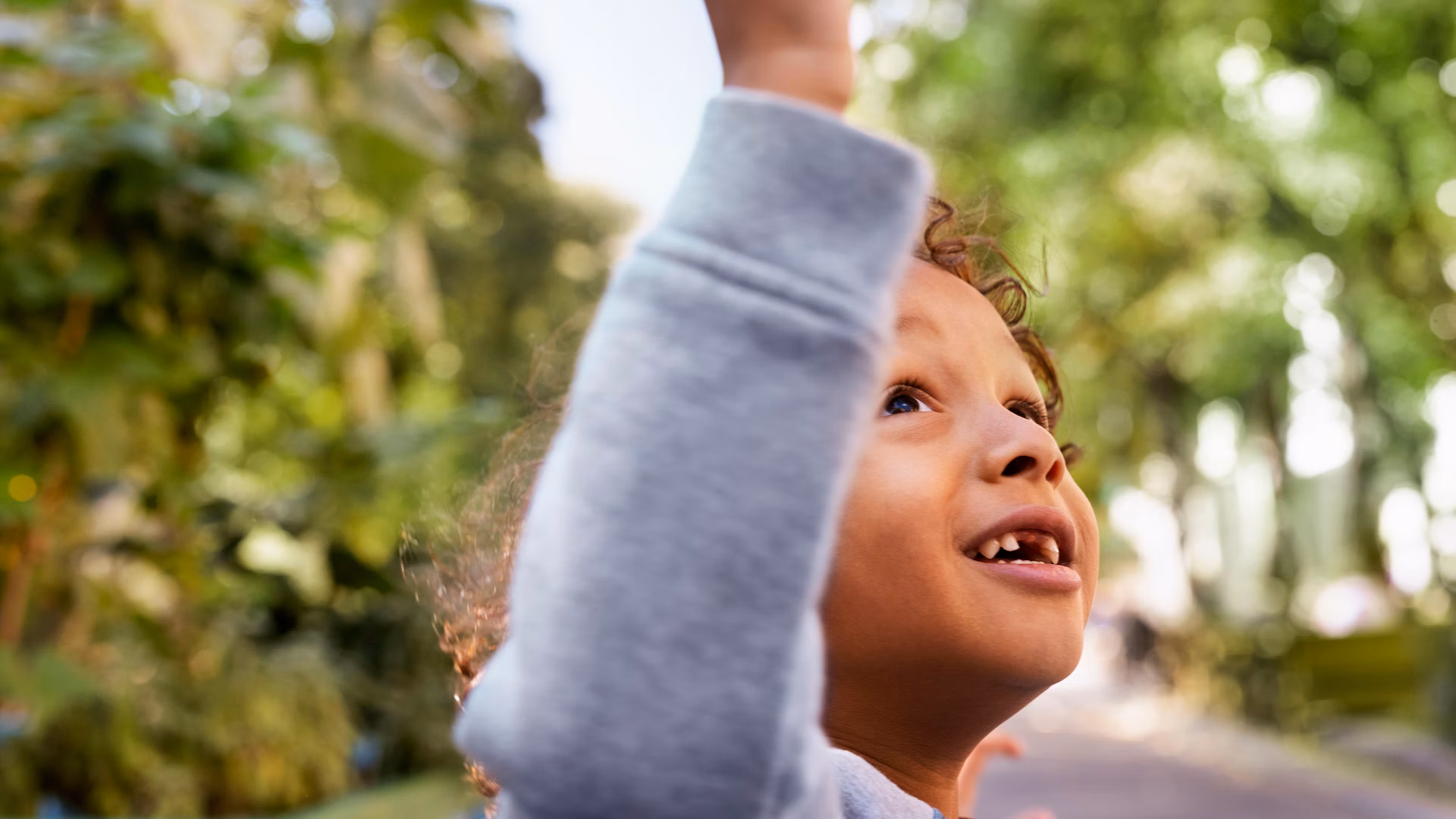 Child outdoors reaches out towards a soap bubble.