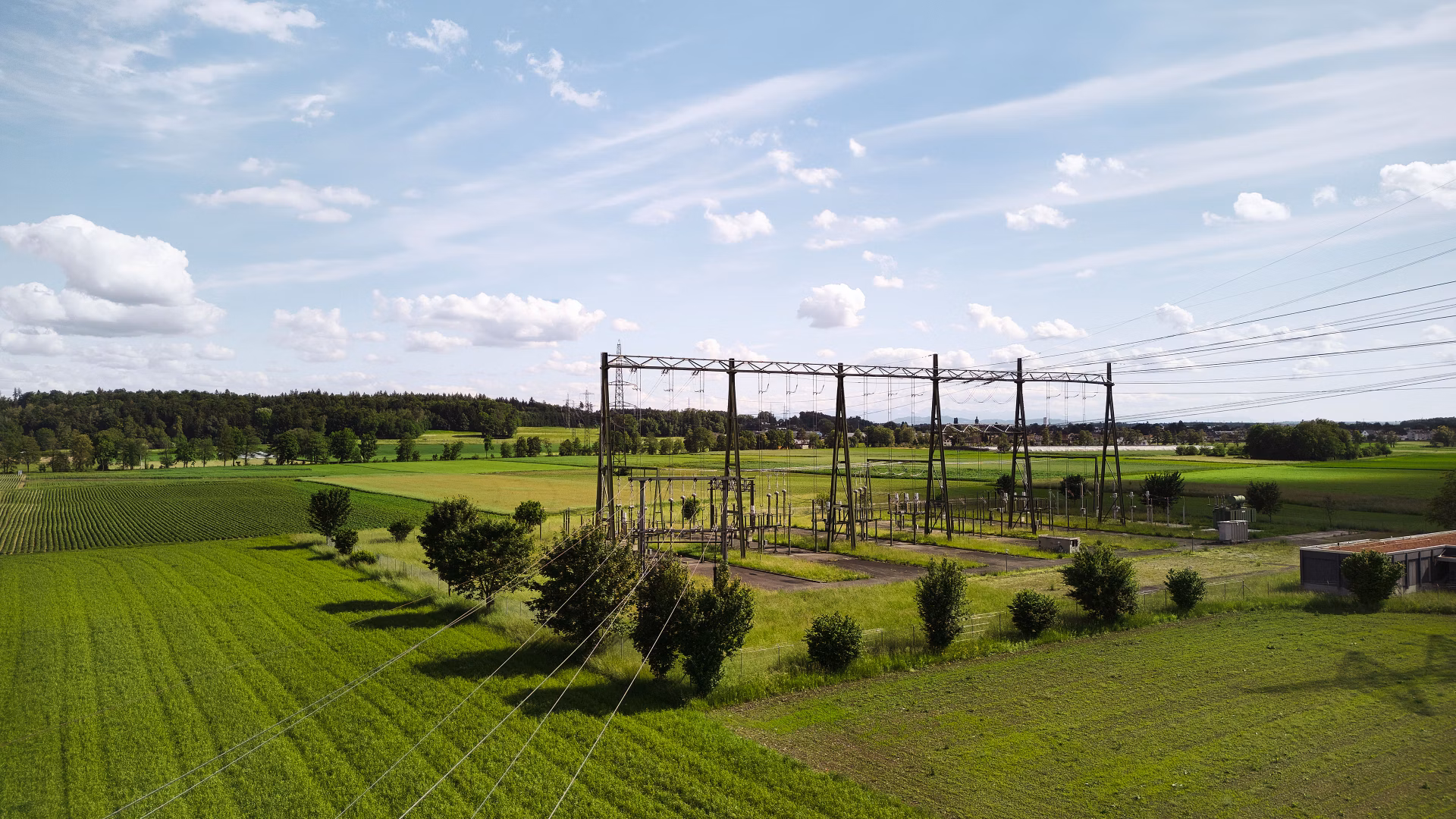 Umspannwerk mit Freileitungen in einer grünen Agrarlandschaft unter blauem Himmel
