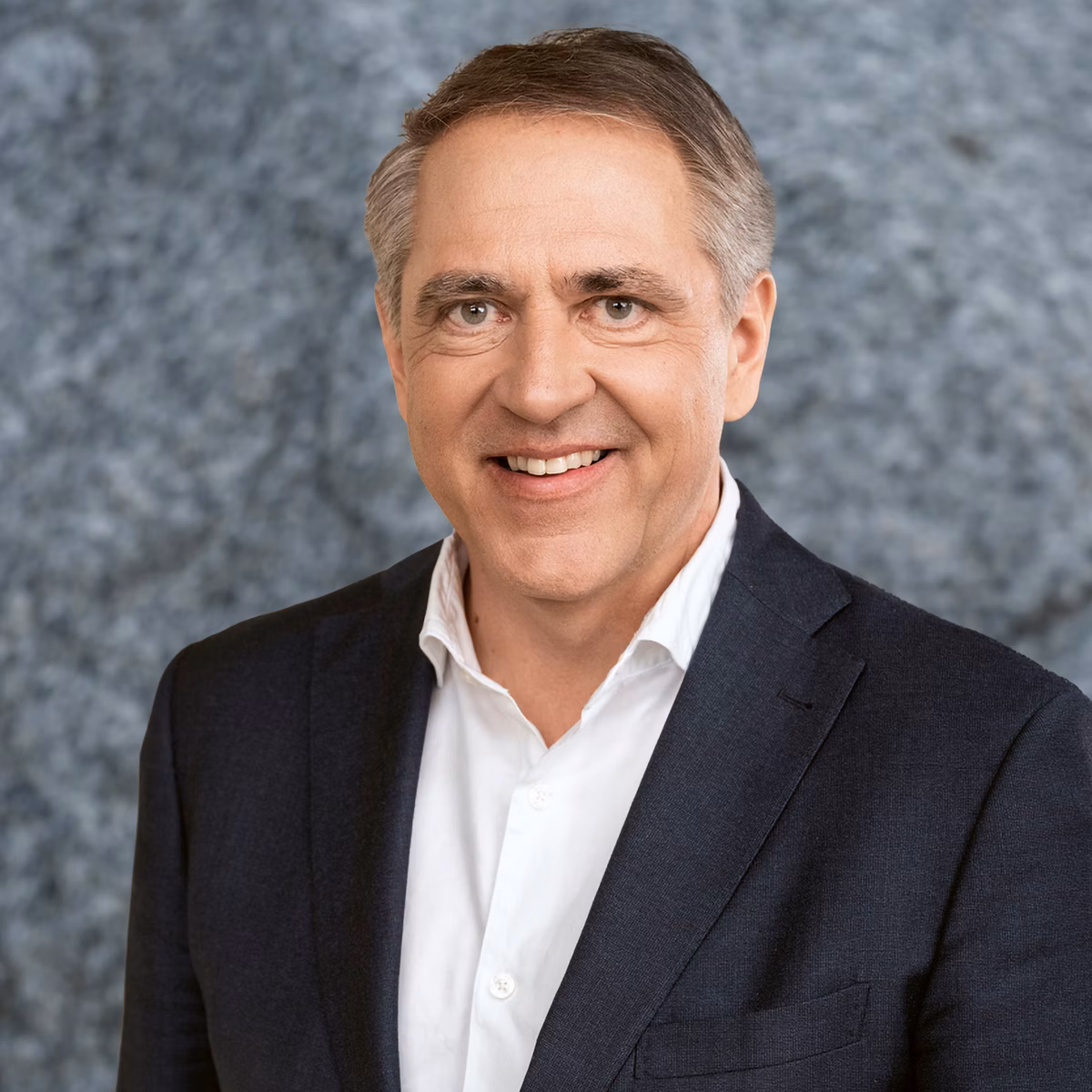 Man in a dark suit and white shirt in front of a grey background