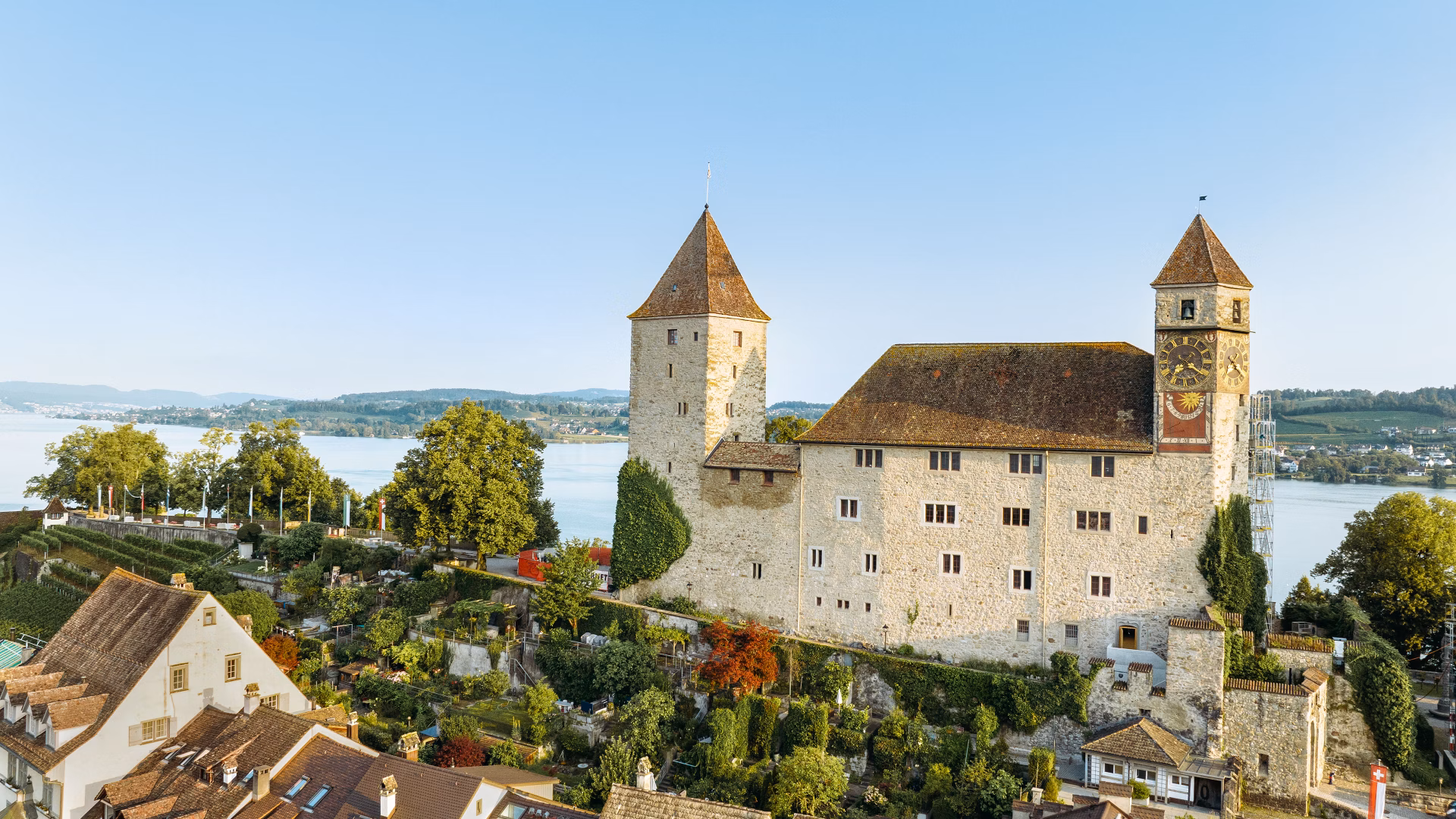 Historisches Schloss auf einem Hügel über Wohnhäusern, Gärten und einem See bei klarem Himmel