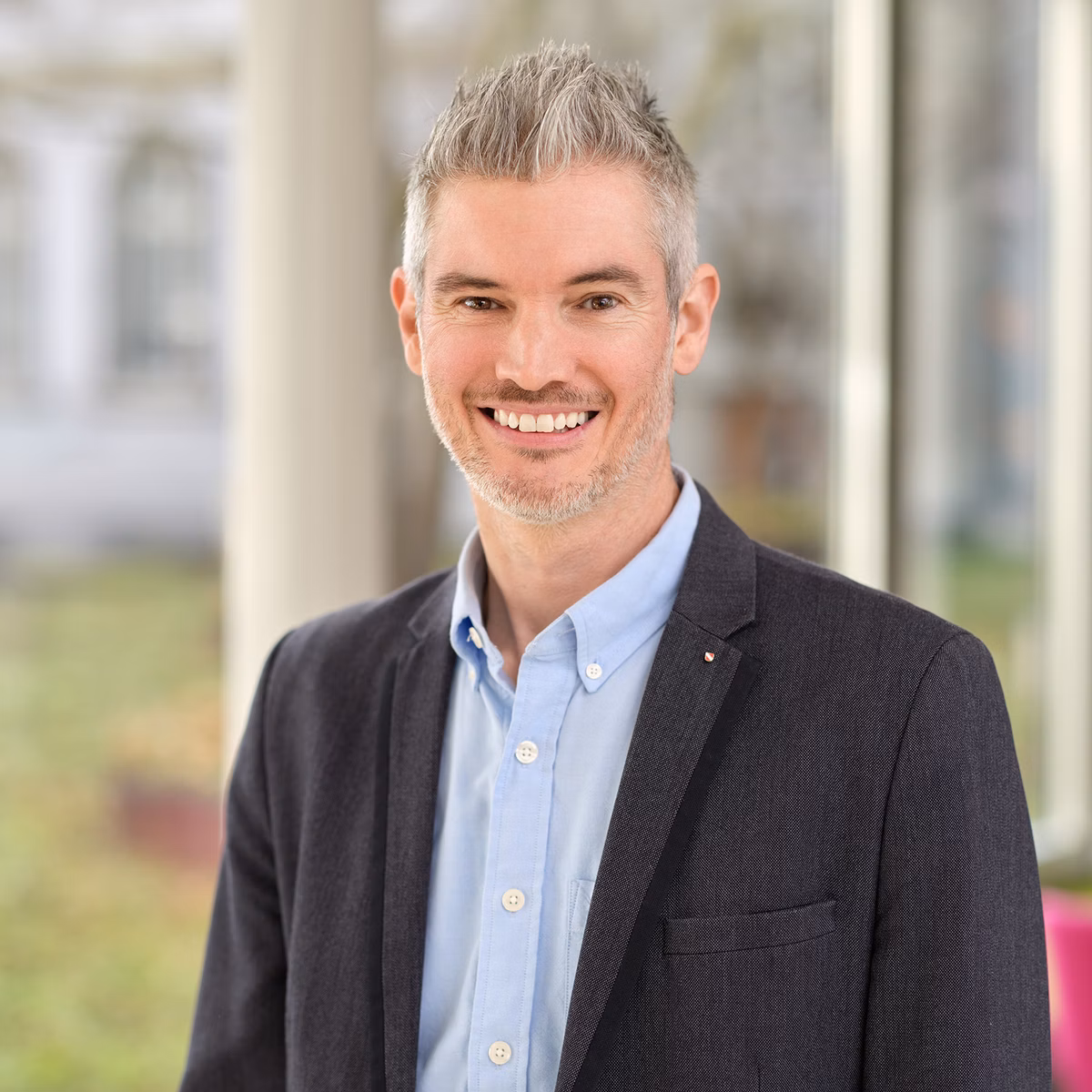 Portrait of a smiling man in a shirt and jacket in front of large windows