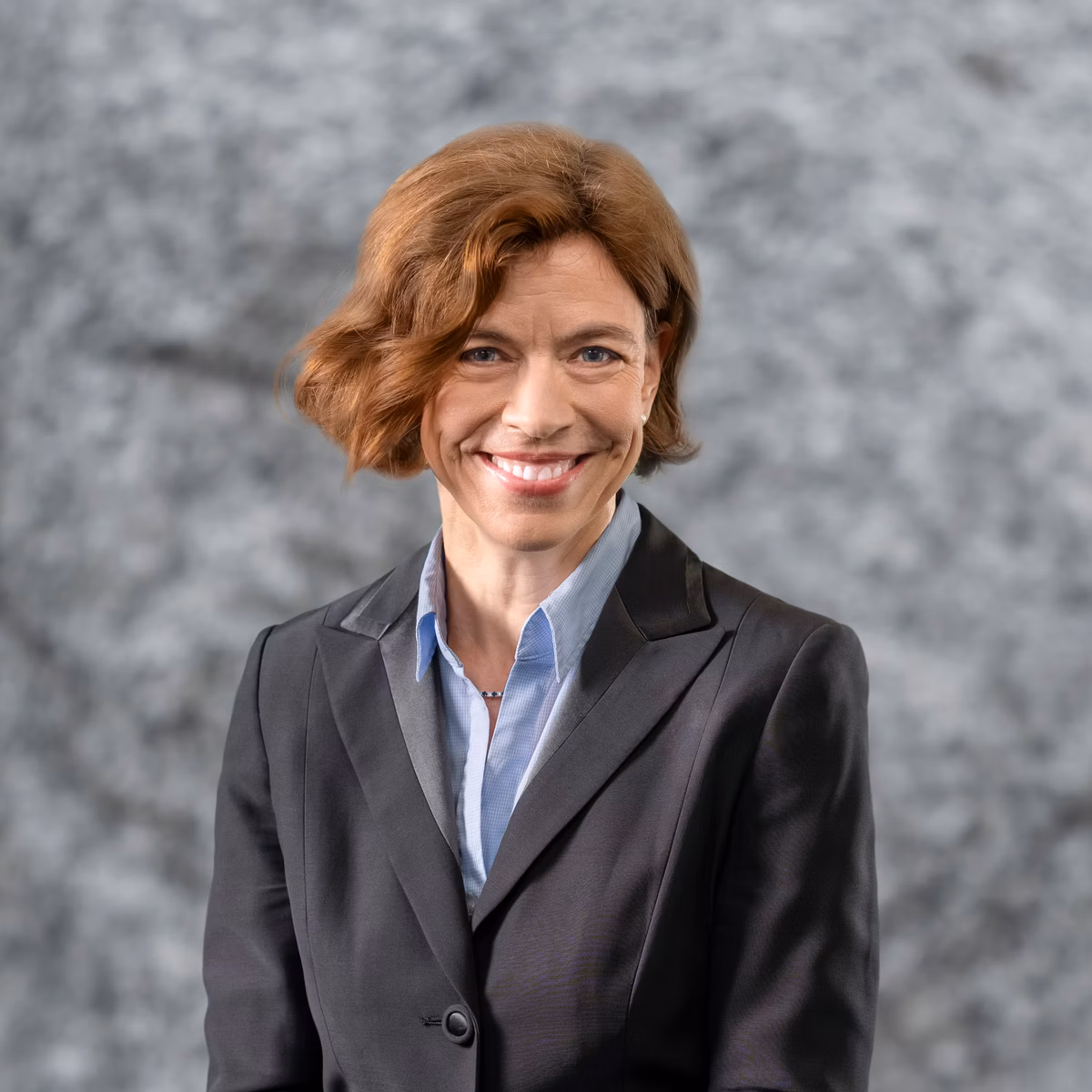 Portrait of a woman in a dark blazer against a grey background