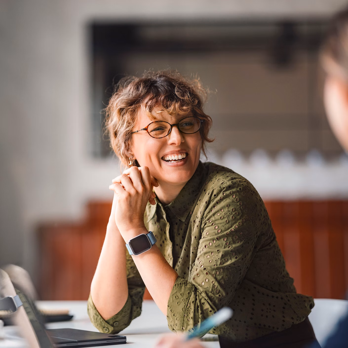 Two people in conversation at a table, a woman wearing glasses smiles.