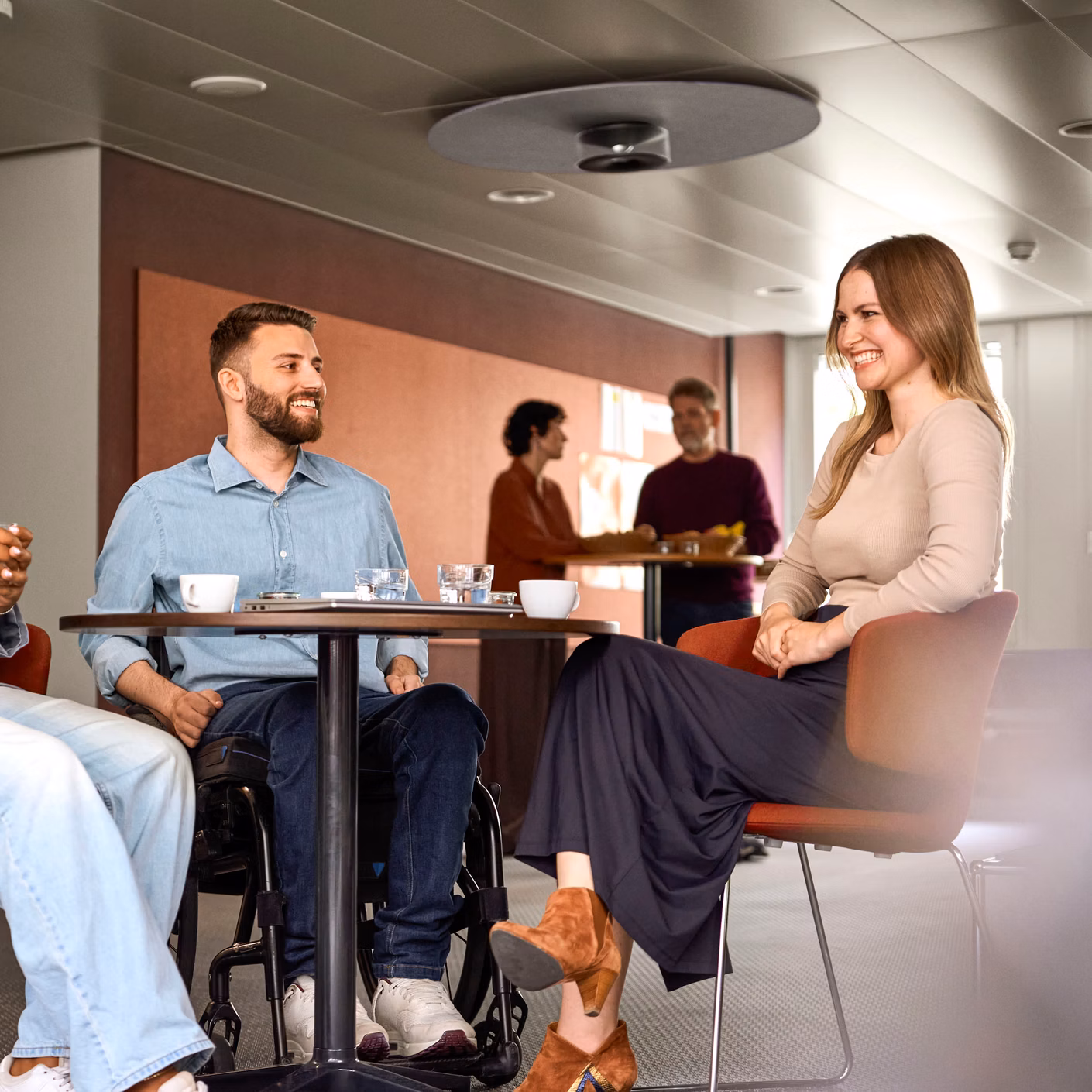 Drei Personen sitzen an einem Tisch in einem modernen Innenraum und unterhalten sich.