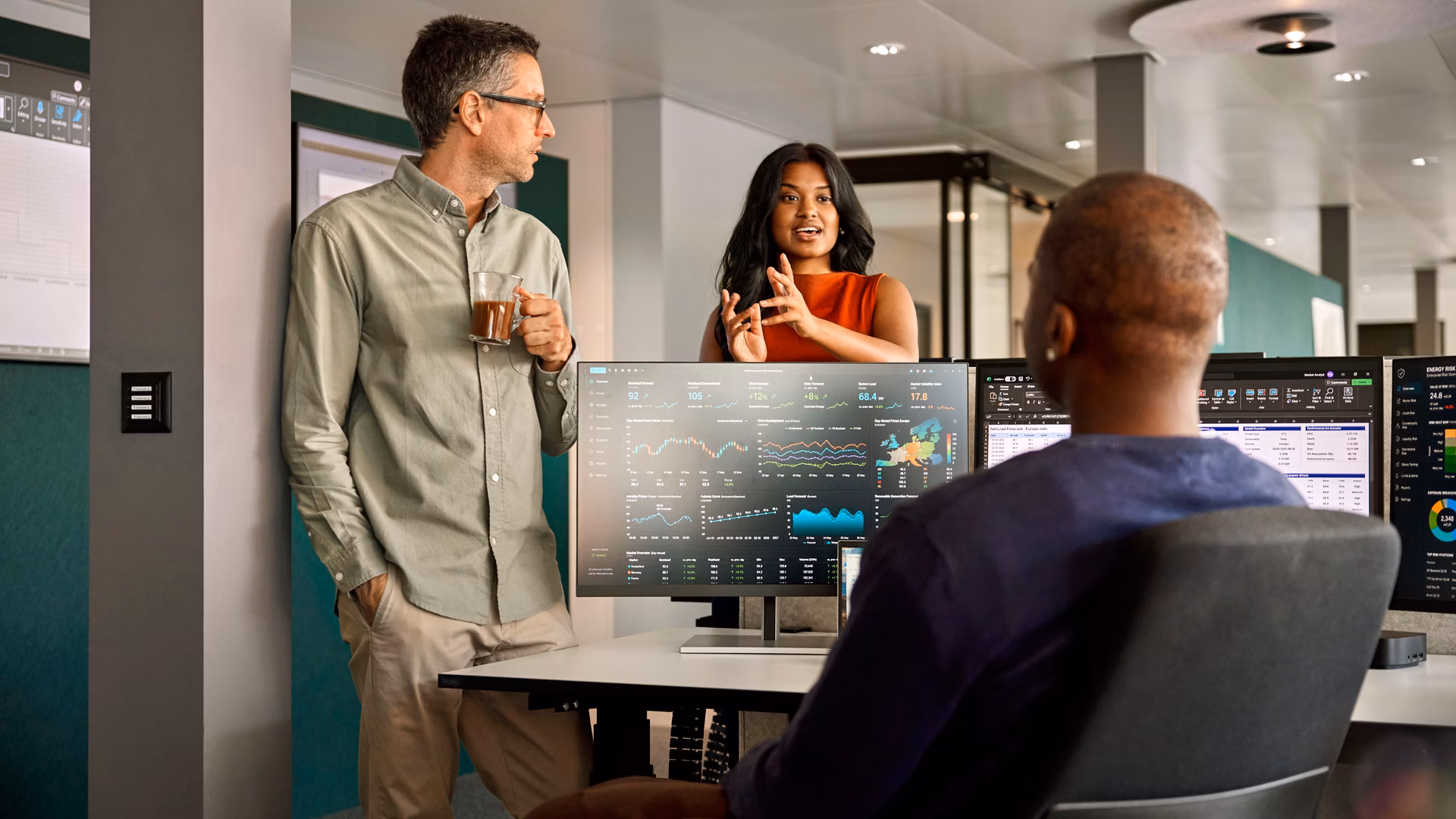 Drei Personen besprechen Datenanalysen an mehreren Bildschirmen in einem modernen Büro.