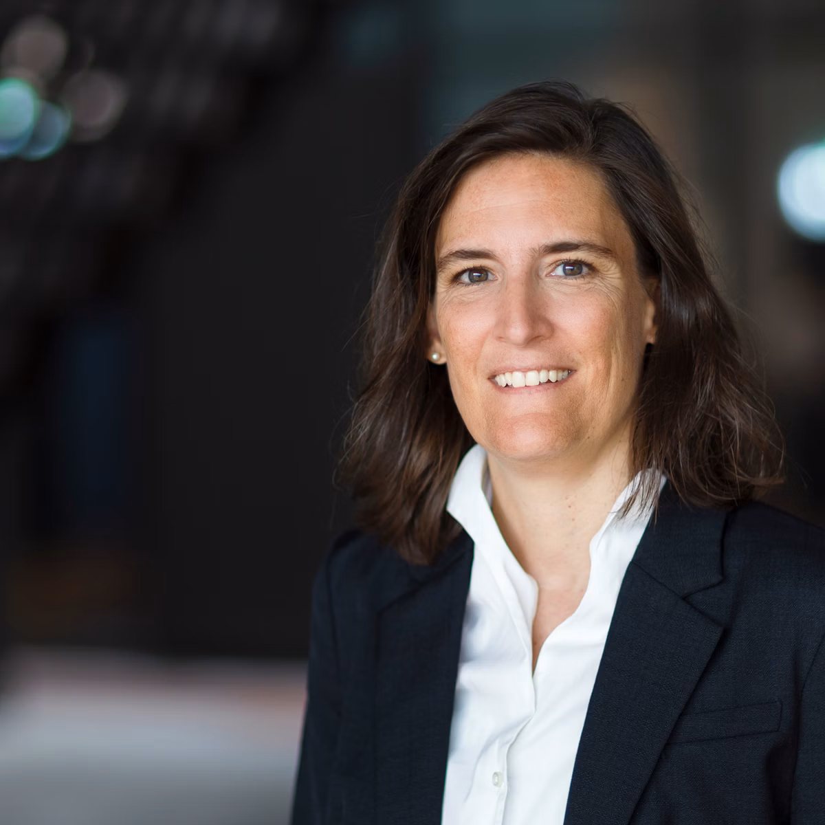 Eliane Kersten in dunklem Blazer und weisser Bluse vor unscharfem Innenraumhintergrund