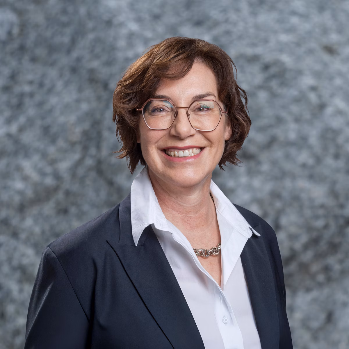 Woman with glasses in a dark blazer against a grey background