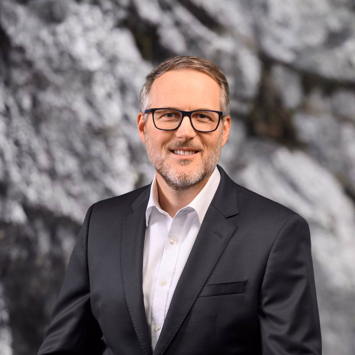 Man in a suit and glasses in front of a rocky background