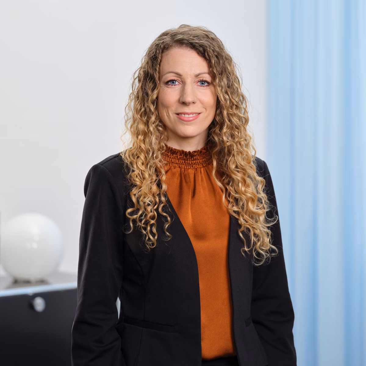 Porträt von Tessa Egli mit lockigem Haar in einem Büro vor hellem Hintergrund