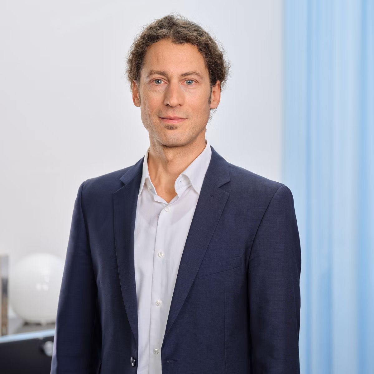 Meik Krauthausen in blauem Blazer und weissem Hemd steht in einem hellen Büro.