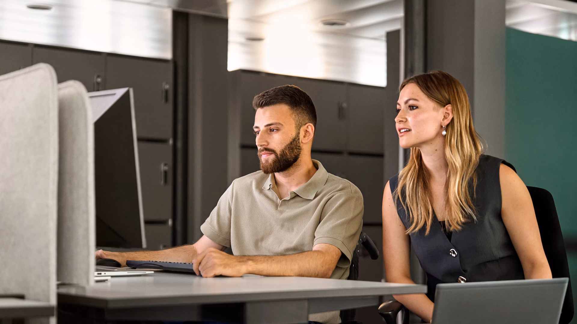 Zwei Personen arbeiten an Laptops in einem modernen Büro.