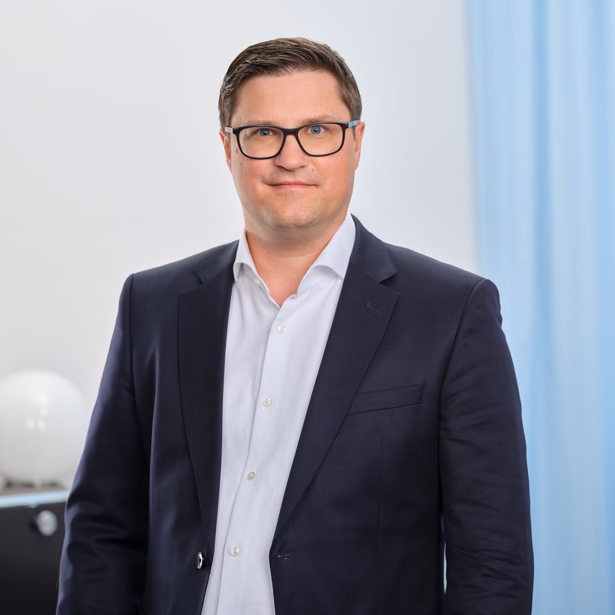 Christian Schürch mit Brille in Anzugjacke und weissem Hemd vor hellem Bürohintergrund